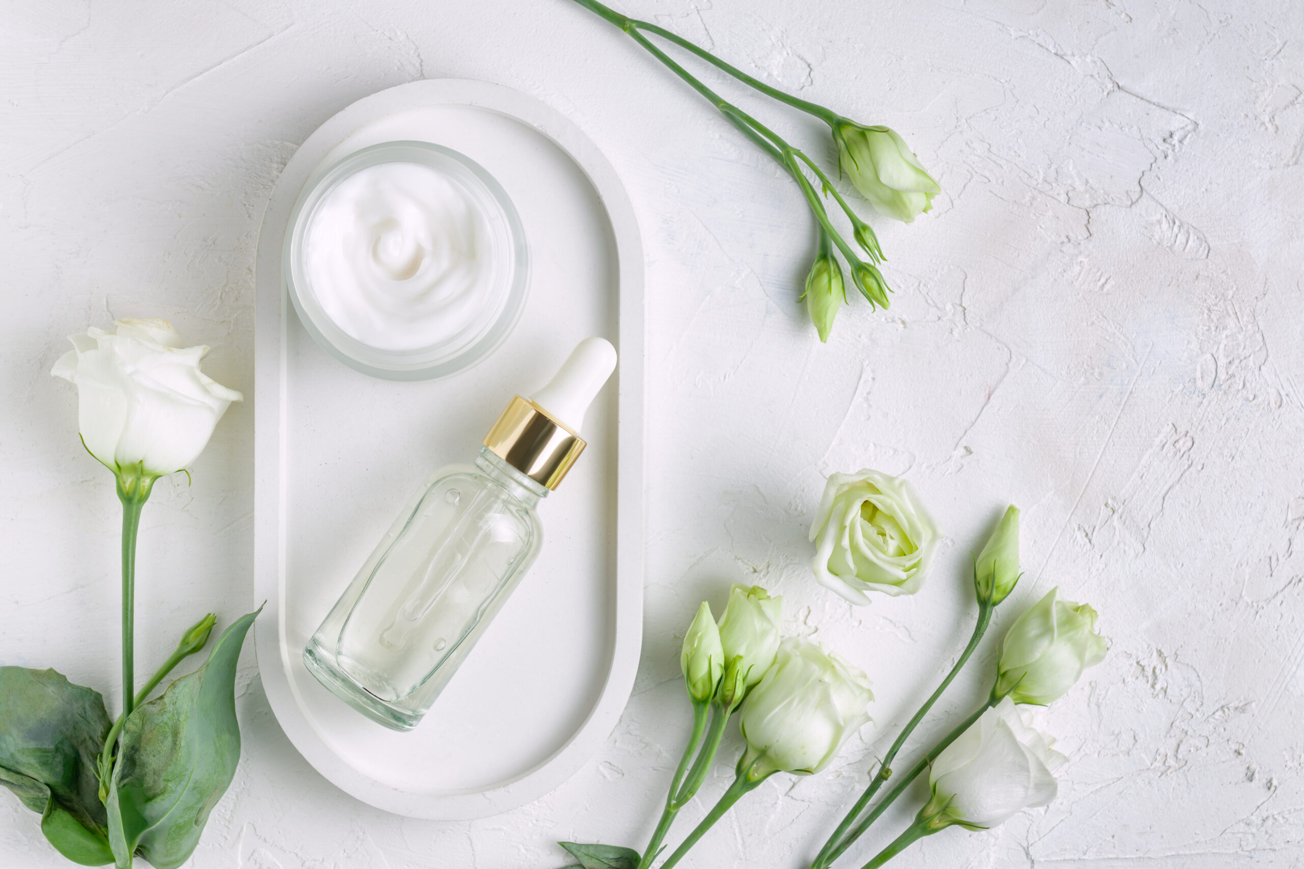 Unbranded bottles in mockup style. Beauty background with facial cosmetic products. Open jar with face cream and dropper bottle with beauty serum on concrete tray. Flat lay